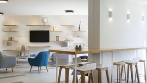 Una sala de estar moderna con un televisor de pantalla plana, estanterías de madera y una zona de comedor con taburetes de bar.
