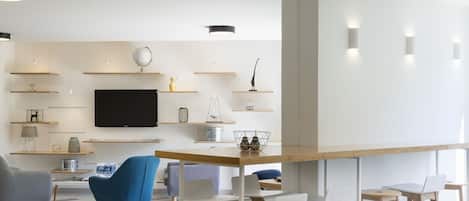 A modern living room with a flat-screen TV, wooden shelves, and a dining area with bar stools.