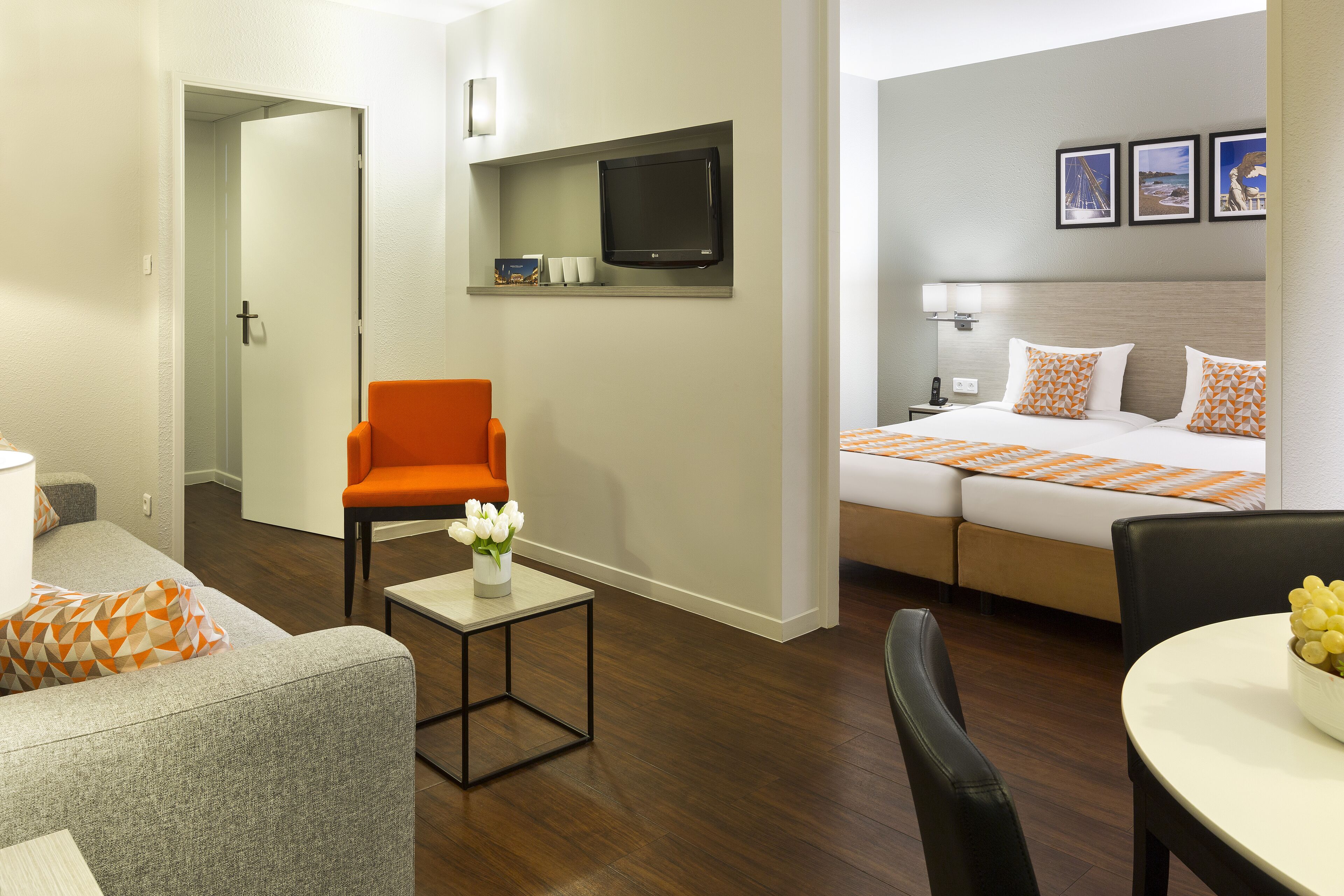 Une chambre d’hôtel comprenant un lit, une télévision, un coin salon avec une chaise et une table, ainsi qu’une petite table ornée d’un vase de fleurs.