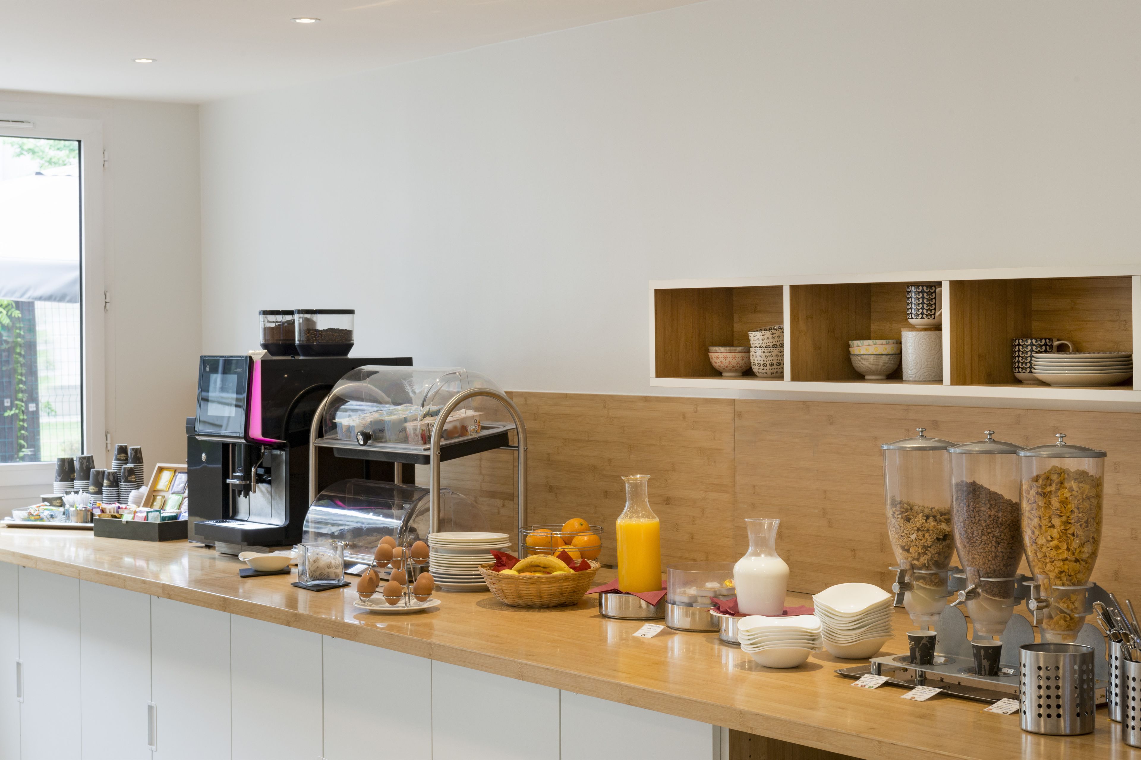 Buffet de café da manhã com máquinas de café, frutas, cereais e dispensadores de leite.