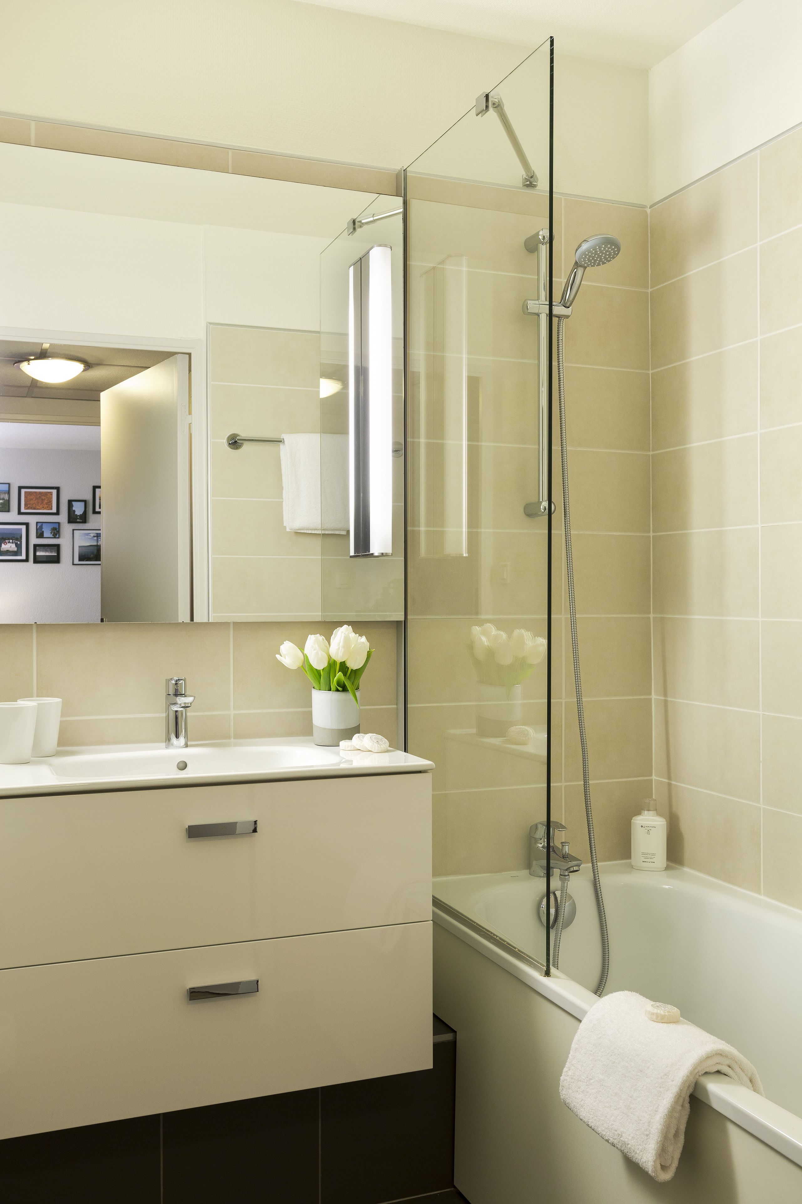 A modern bathroom with a glass-enclosed shower, a white sink with a vase of flowers, and a bathtub with a towel.
