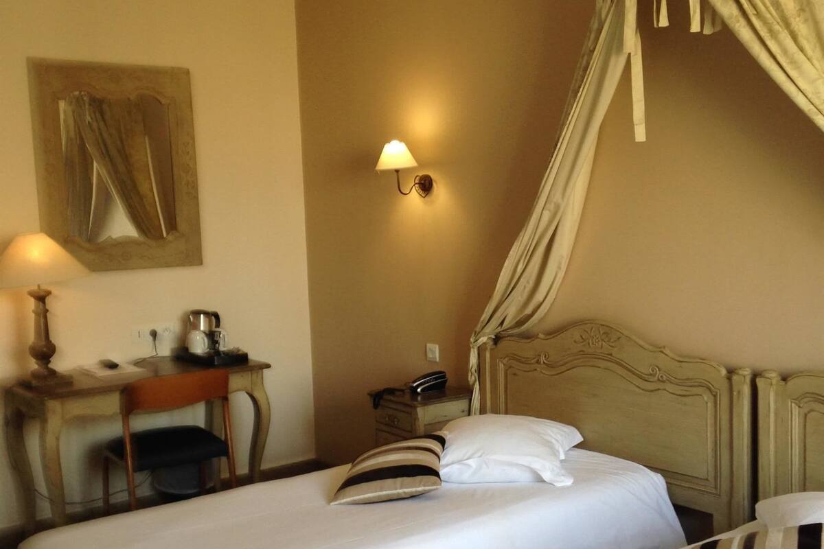 Une chambre d’hôtel avec deux lits, un bureau avec une lampe, une table de chevet et une lampe fixée au mur.