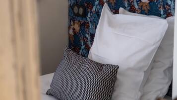 A bed with white linens and patterned pillows, set against a floral-patterned headboard.