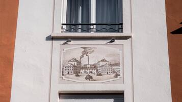 A building facade with two windows, one with a balcony and a mural depicting a historical scene.