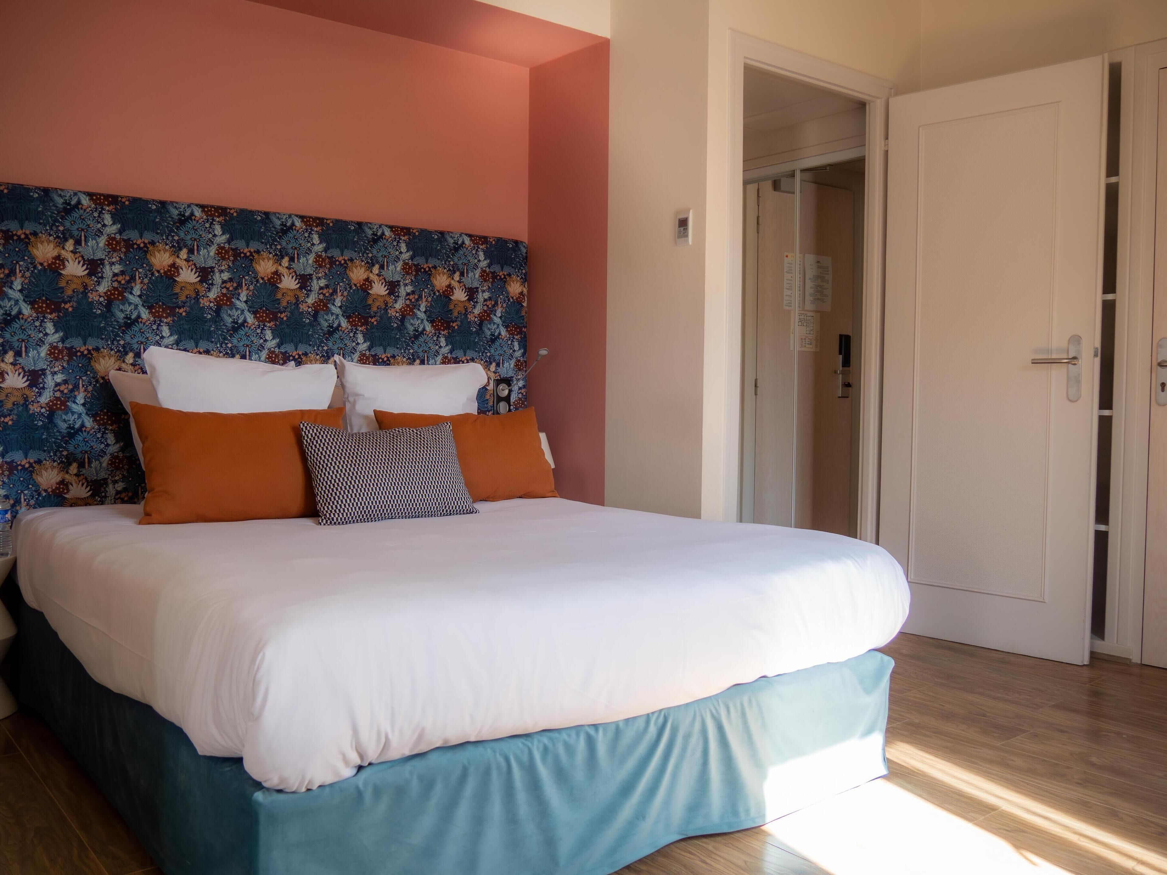 A neatly made bed with white and blue bedding, a floral headboard, and a door to the right.