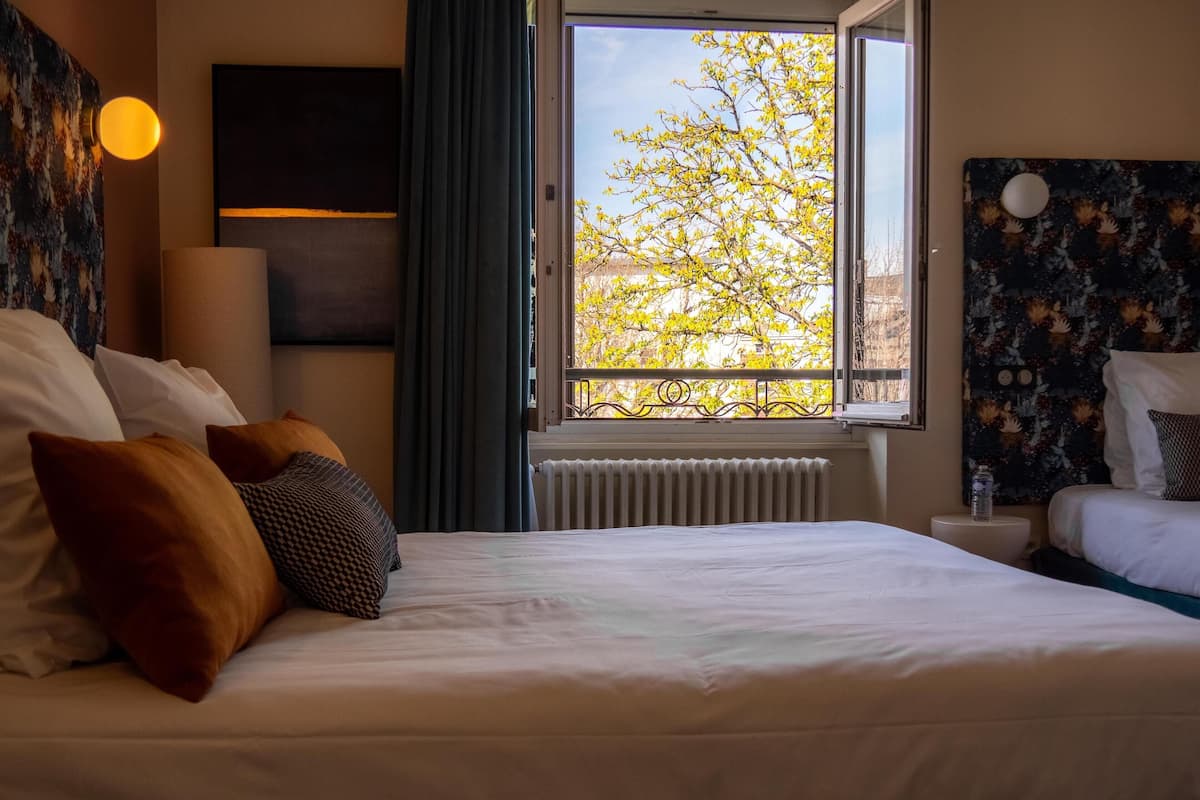 Une chambre d’hôtel avec un grand lit, une fenêtre donnant sur des arbres, un radiateur et un téléviseur fixé au mur.