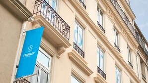 A multi-story building with a beige facade, multiple balconies with wrought iron railings, and a blue banner with the word "STANLEY" on the left side. - Hotel Stanley by HappyCulture (Nancy)