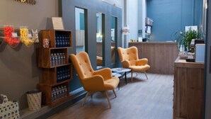 A modern interior with wooden shelves, two yellow armchairs, and a reception desk. - Hotel Stanley by HappyCulture (Nancy)