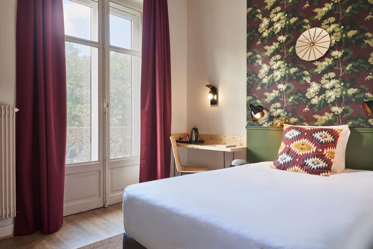 Una habitación de hotel con cama, escritorio y ventana con cortinas.
