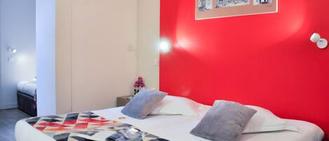 Un dormitorio con una pared de acento roja, una cama con colcha de diseño geométrico y un marco de pared con el nombre "NANCY".