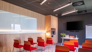 A conference room with red chairs, a whiteboard, a flat-screen TV, and a wooden accent wall. - Ibis Nantes Nord Treillières (Treillieres)