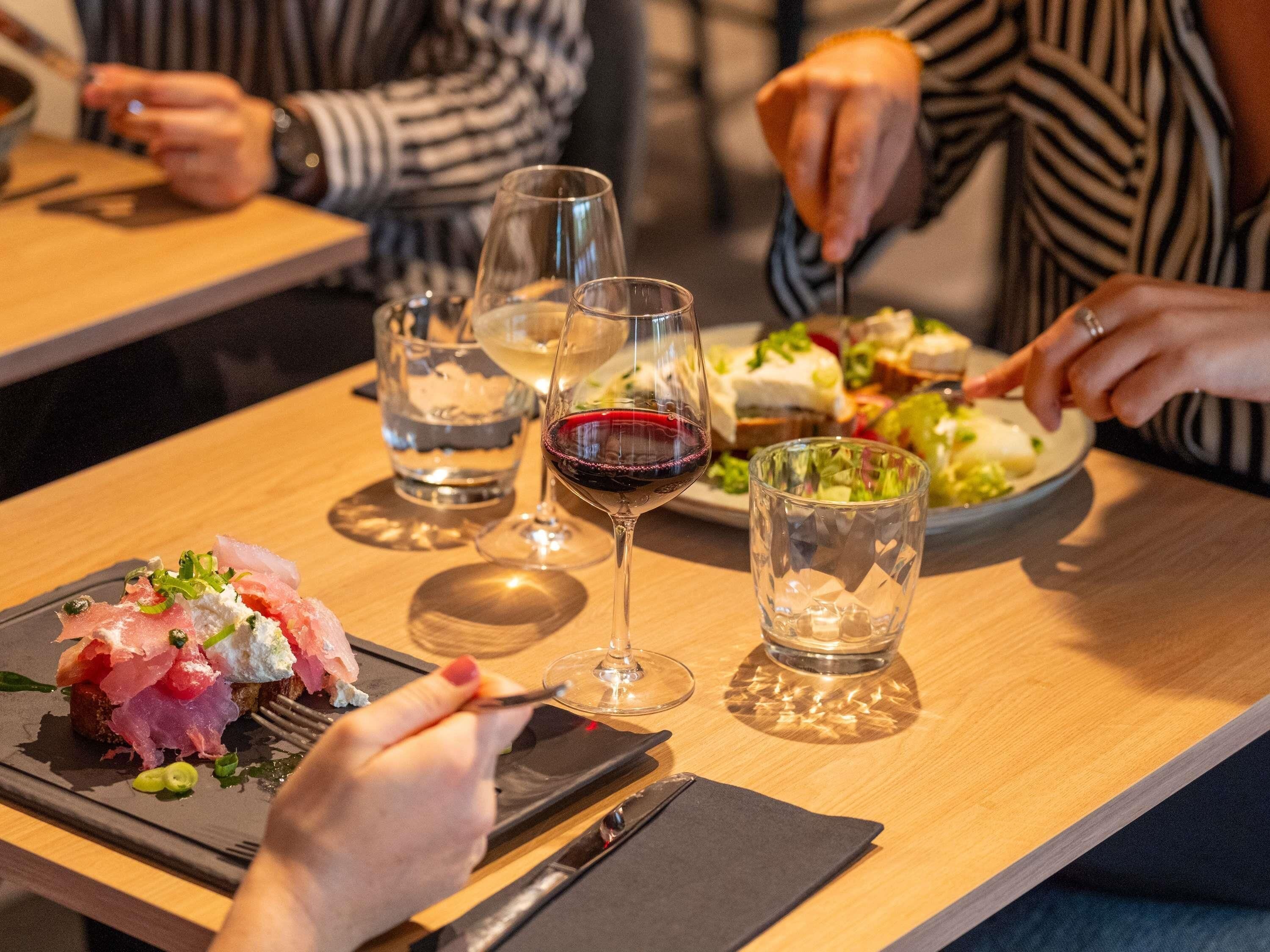 A dining table with plates of food, glasses of water and wine, and a person using a fork.