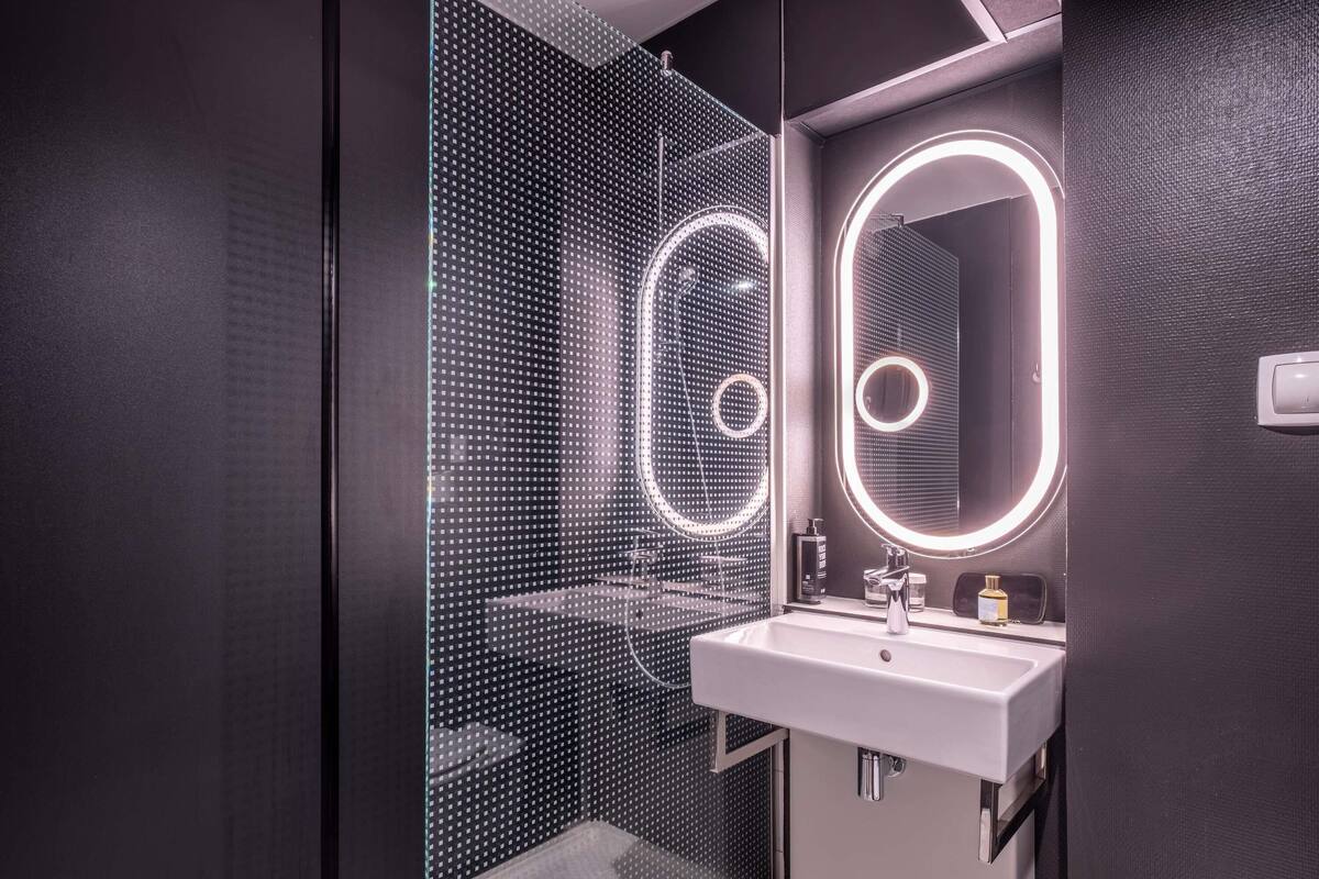 Une salle de bain moderne dotée d’une douche à parois de verre, d’un lavabo blanc et d’un miroir avec des anneaux lumineux.