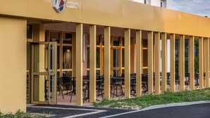 A building with a sign reading 'Albert's Place,' featuring a glass entrance, outdoor seating area with tables and chairs, and a clear sky. - Ibis Nantes Nord Treillières (Treillieres)