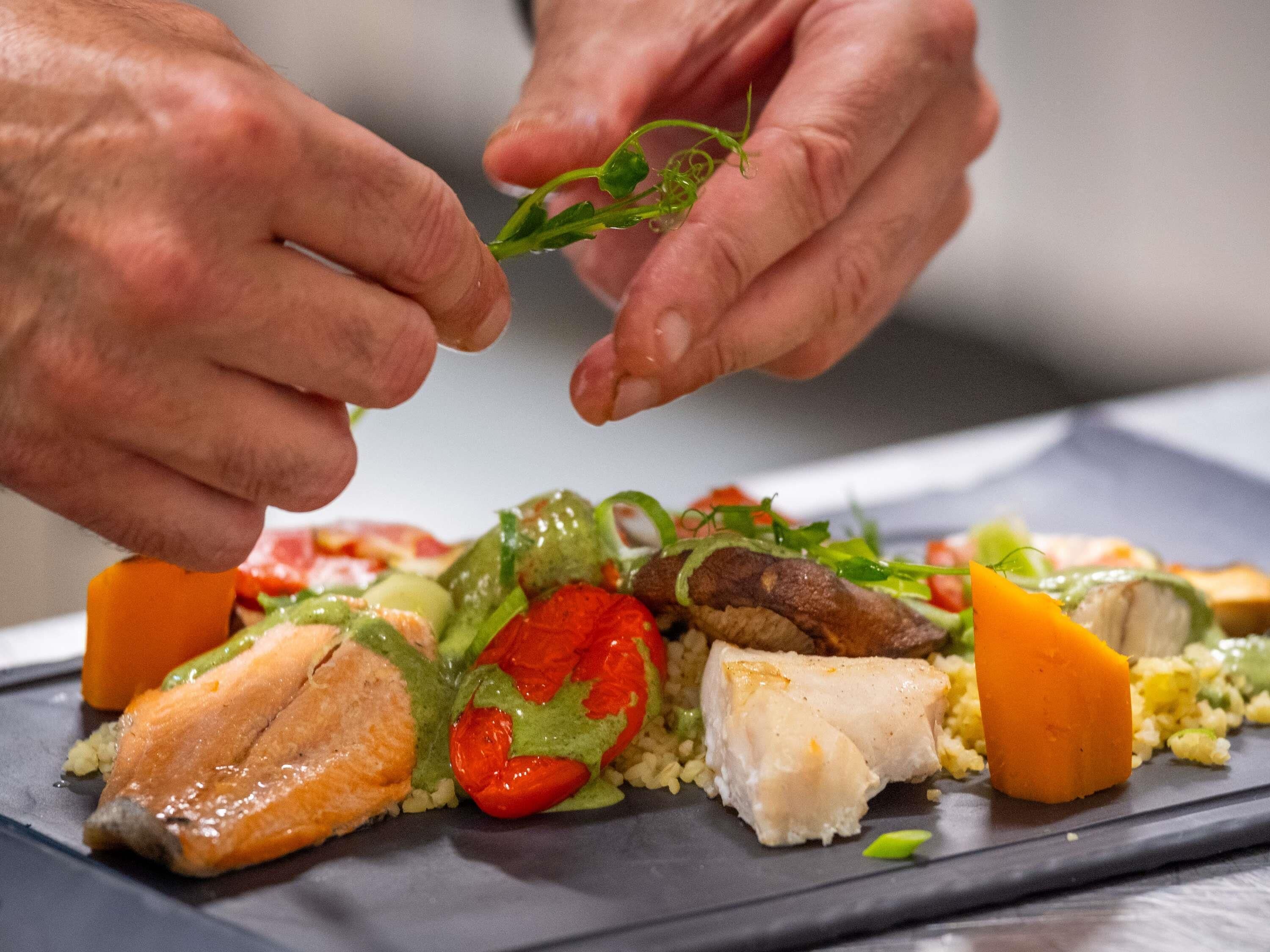 A person placing a green leaf on a dish with various food items.