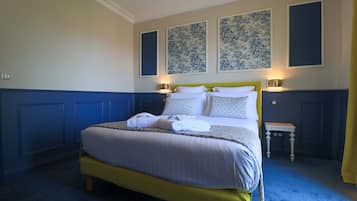 A neatly made bed with white linens and patterned pillows, a bedside table with a lamp, and blue and yellow wall paneling.
