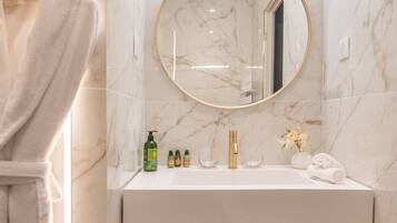 Une salle de bain avec un mur en marbre, un miroir rond, un lavabo blanc et un porte-serviettes.