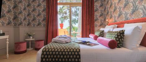 A hotel room with a large bed, a small table with a vase, and a window with curtains.