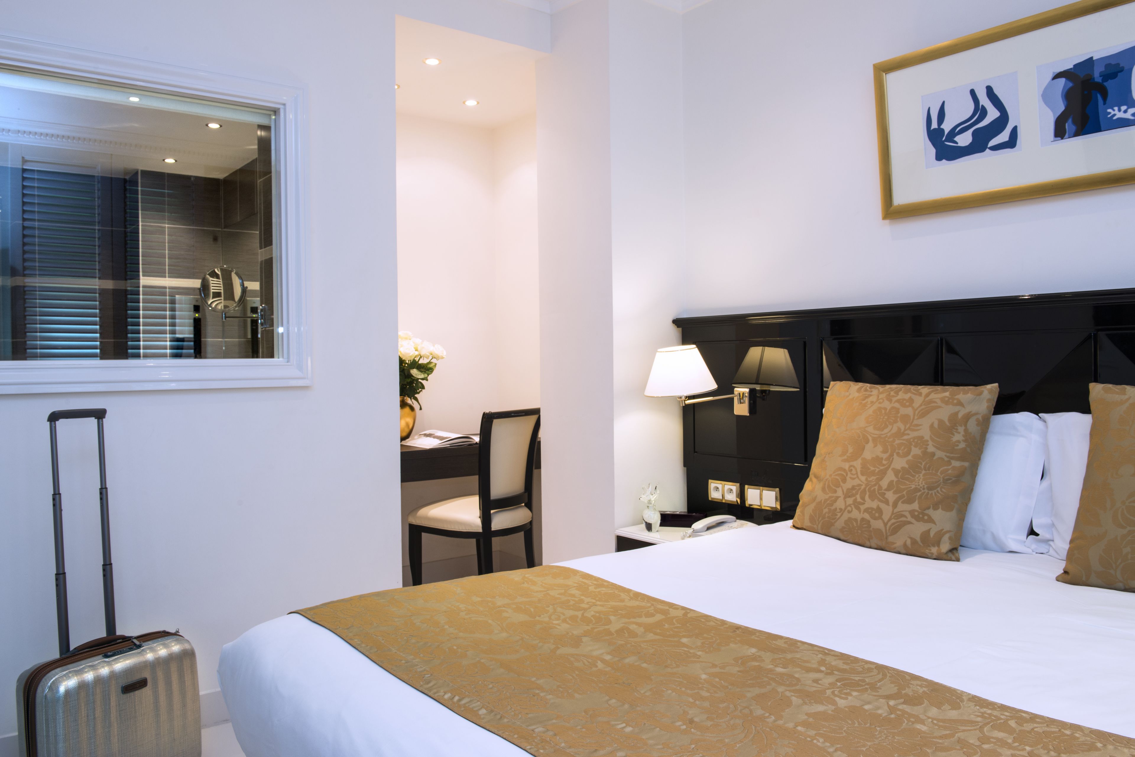 Una habitación de hotel con cama, escritorio, silla, lámpara y ventana con persianas.