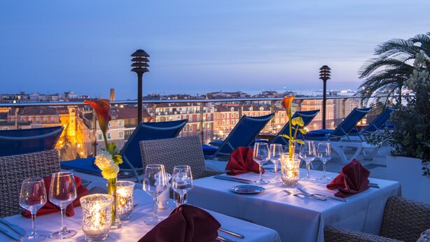 A rooftop dining area with tables set for two, featuring clear glassware, candles, and a city view. - Hôtel Aston La Scala (Nice)