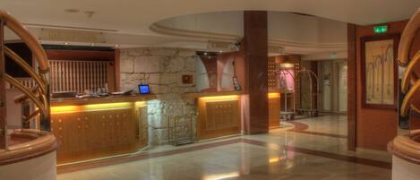 Un vestíbulo de hotel con una recepción, una pared de piedra y un espejo grande.