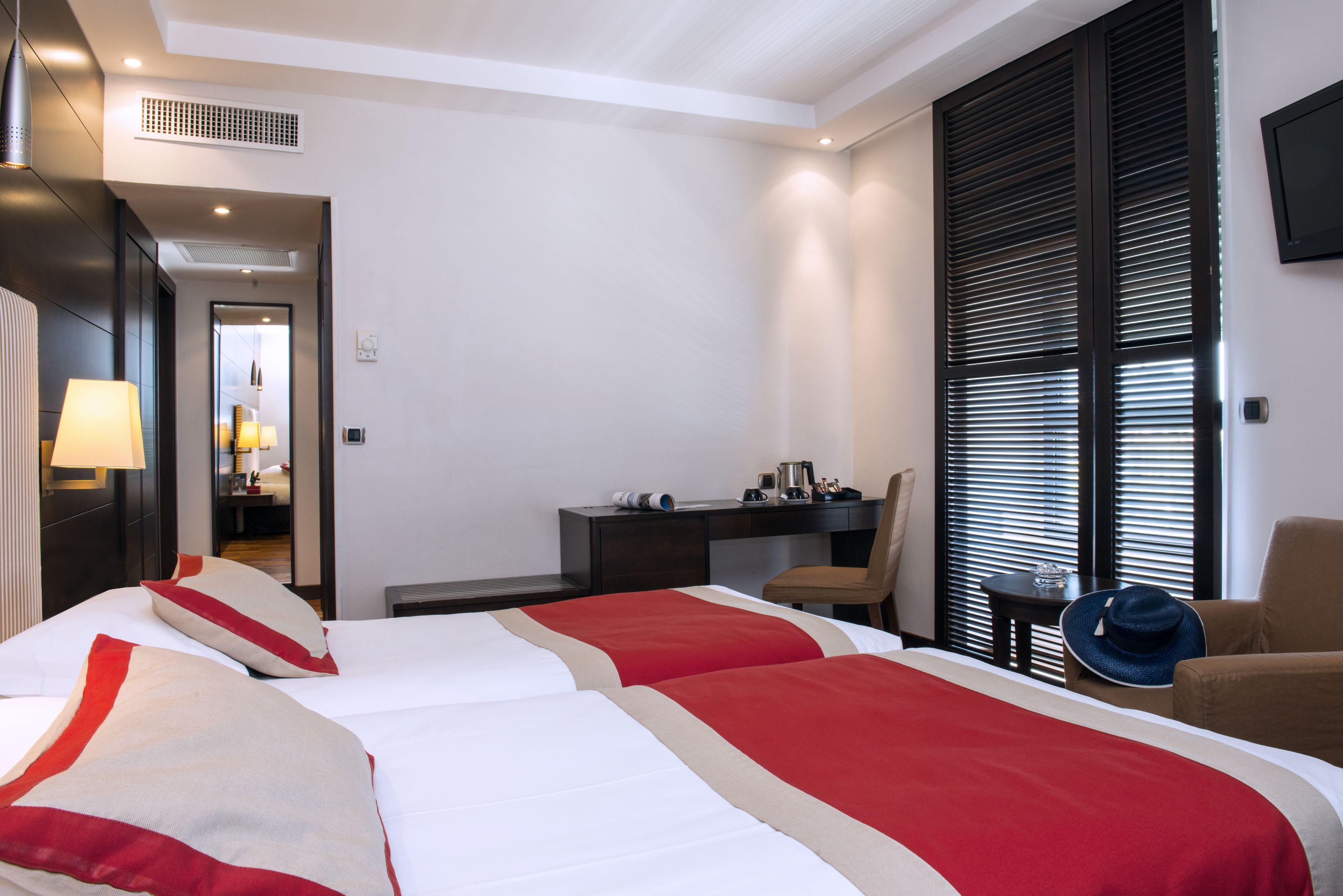 A hotel room with two beds, a desk, a chair, and a TV.