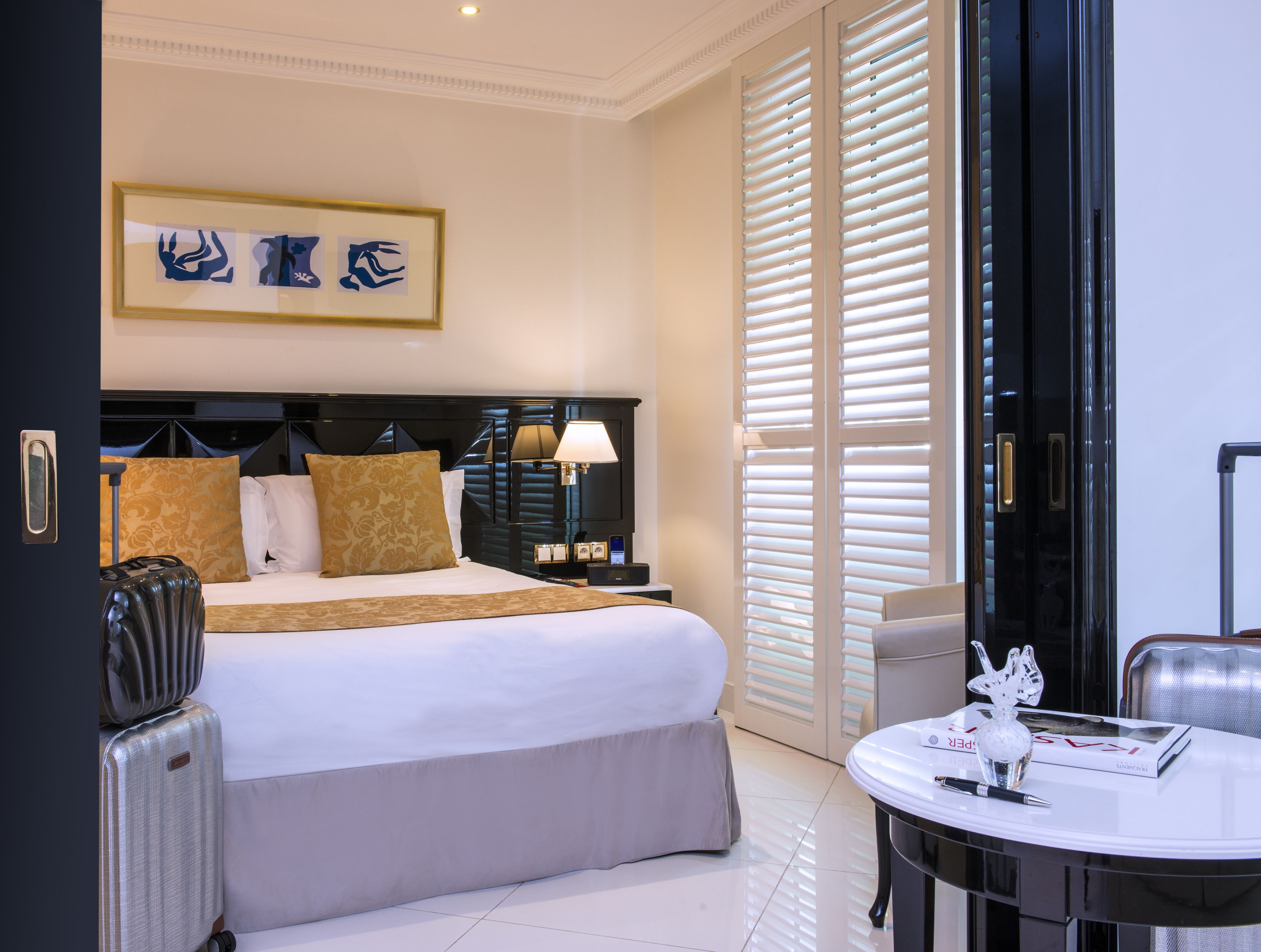 Een hotelkamer met een bed, nachtkastje, lamp en uitzicht op buiten door grote ramen.