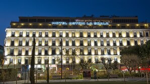 A multi-story hotel with a classic facade, illuminated signage, and a well-maintained outdoor area with benches and trees. - Hôtel Aston La Scala (Nice)
