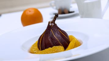 A white plate with a pear on a bed of yellow fruit, a white cup, and a white pitcher on a table.