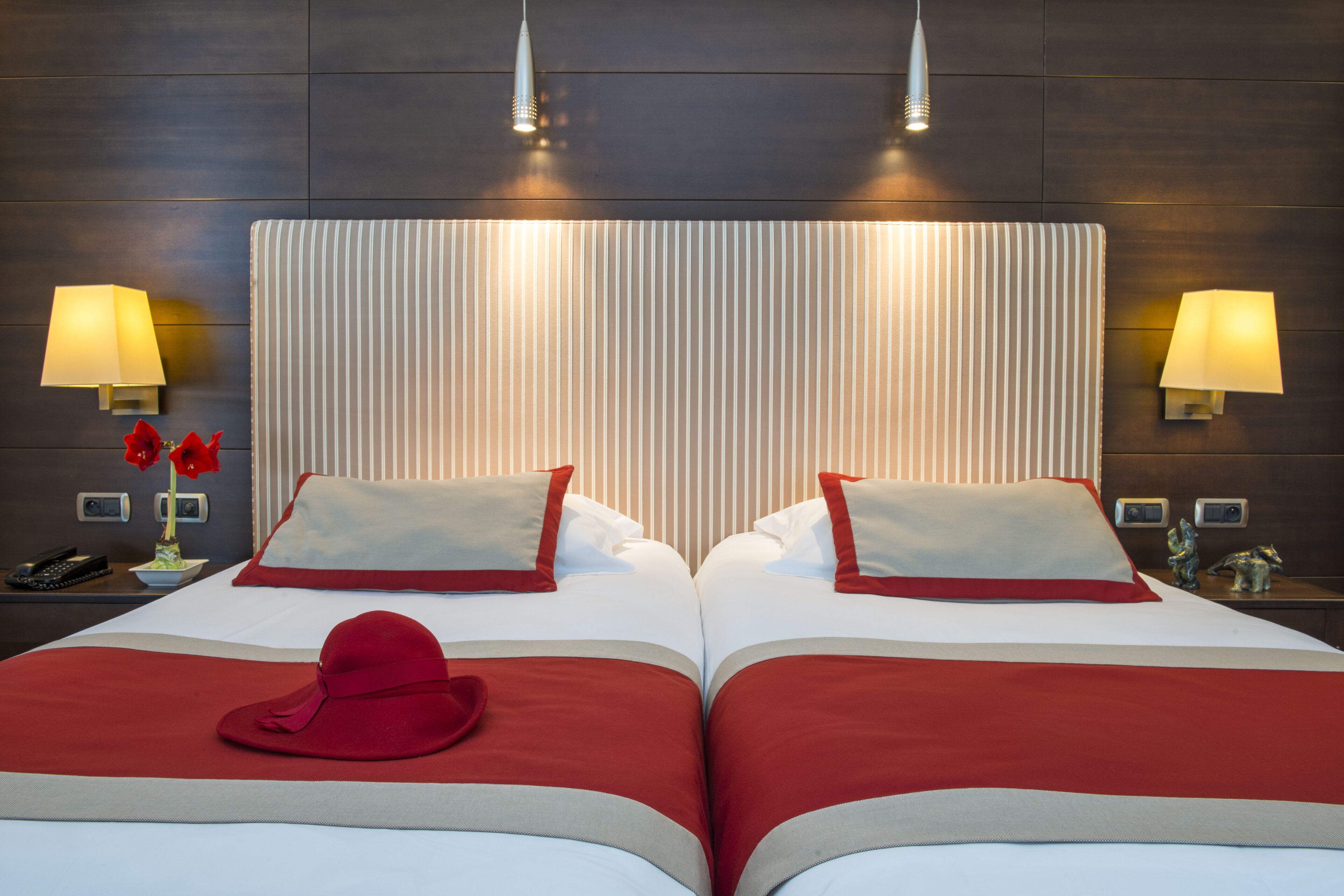 A hotel room with a large bed, two bedside lamps, a telephone, and a decorative vase with flowers.