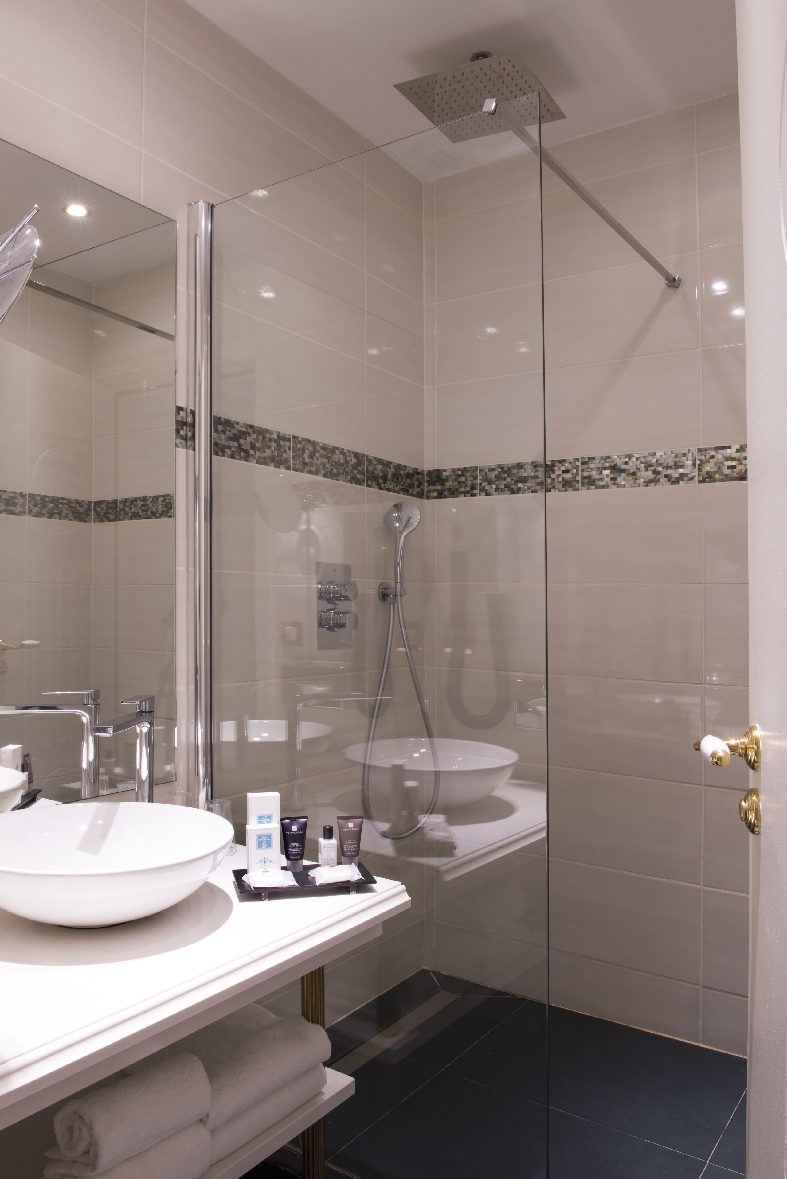 A modern bathroom with a glass-enclosed shower, a white sink, and a vanity with toiletries.