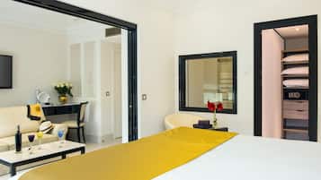 Quarto de hotel com cama, escrivaninha, cadeira, televisão e guarda-roupa.