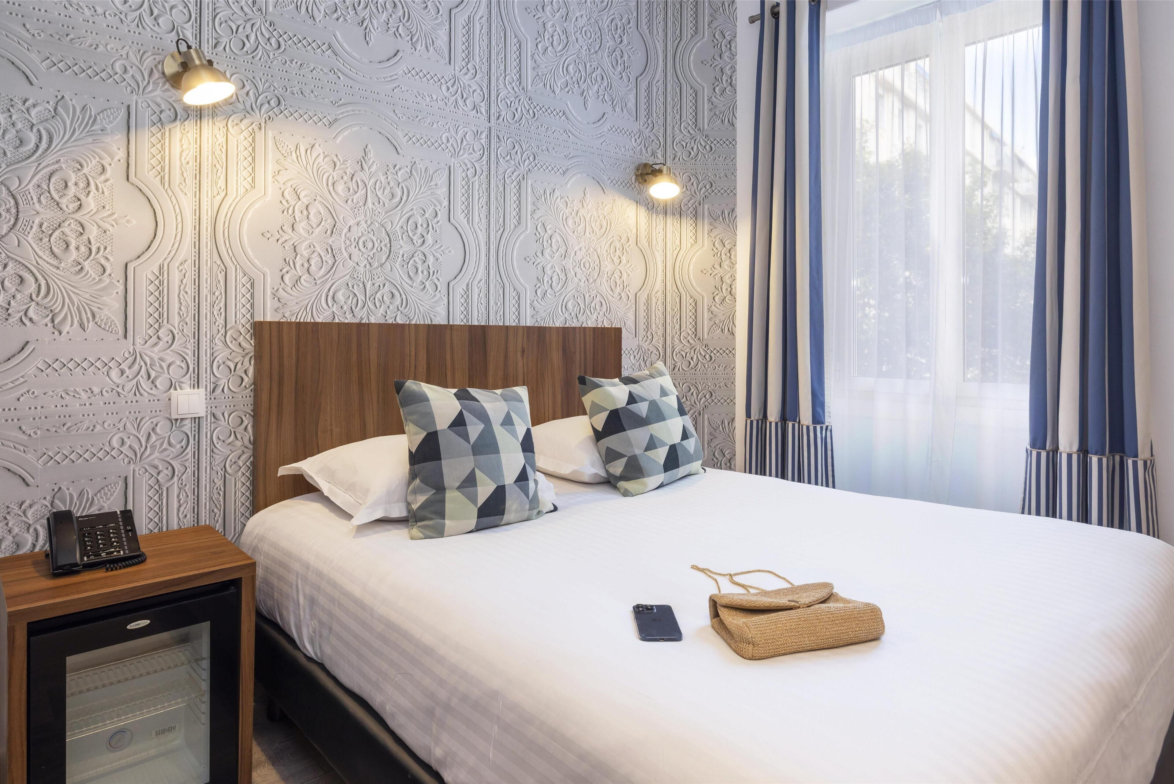A neatly made bed with patterned pillows, a bedside phone, and a smartphone on the nightstand.