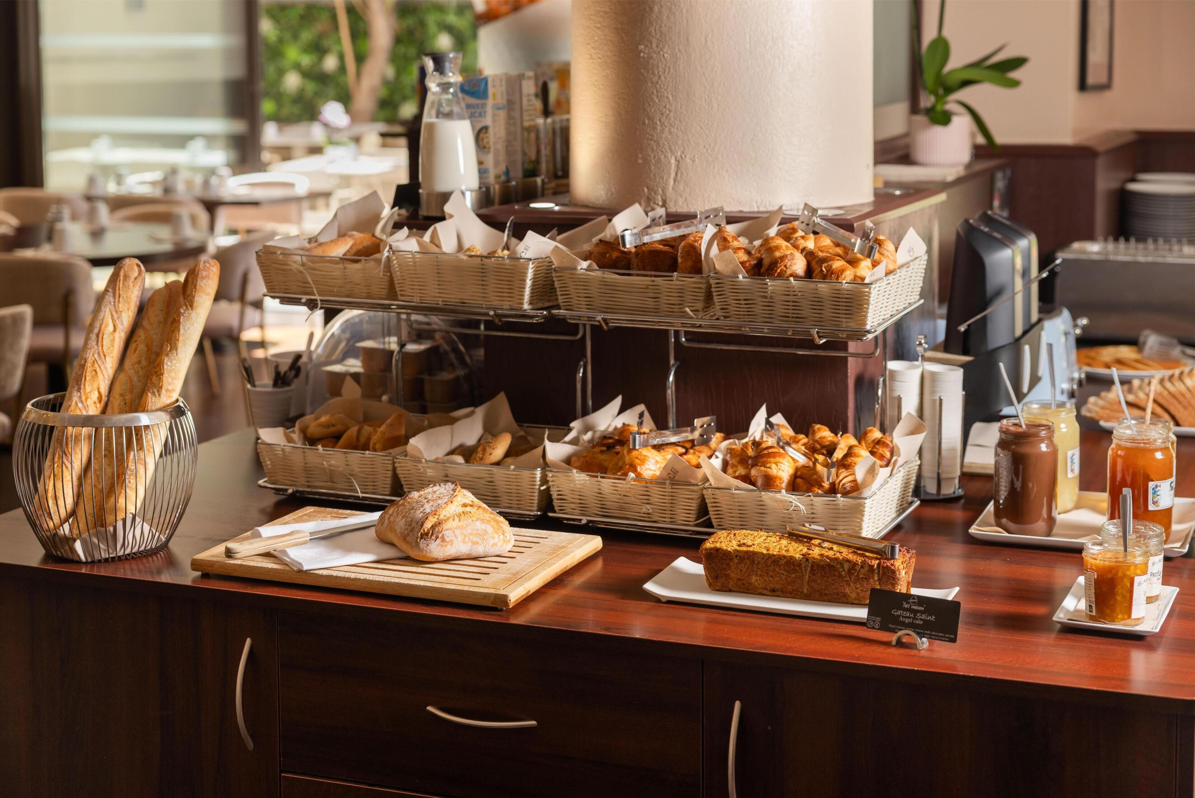 Un comptoir de buffet proposant une variété de pains, de viennoiseries, et un panneau indiquant la présence d’options sans gluten.