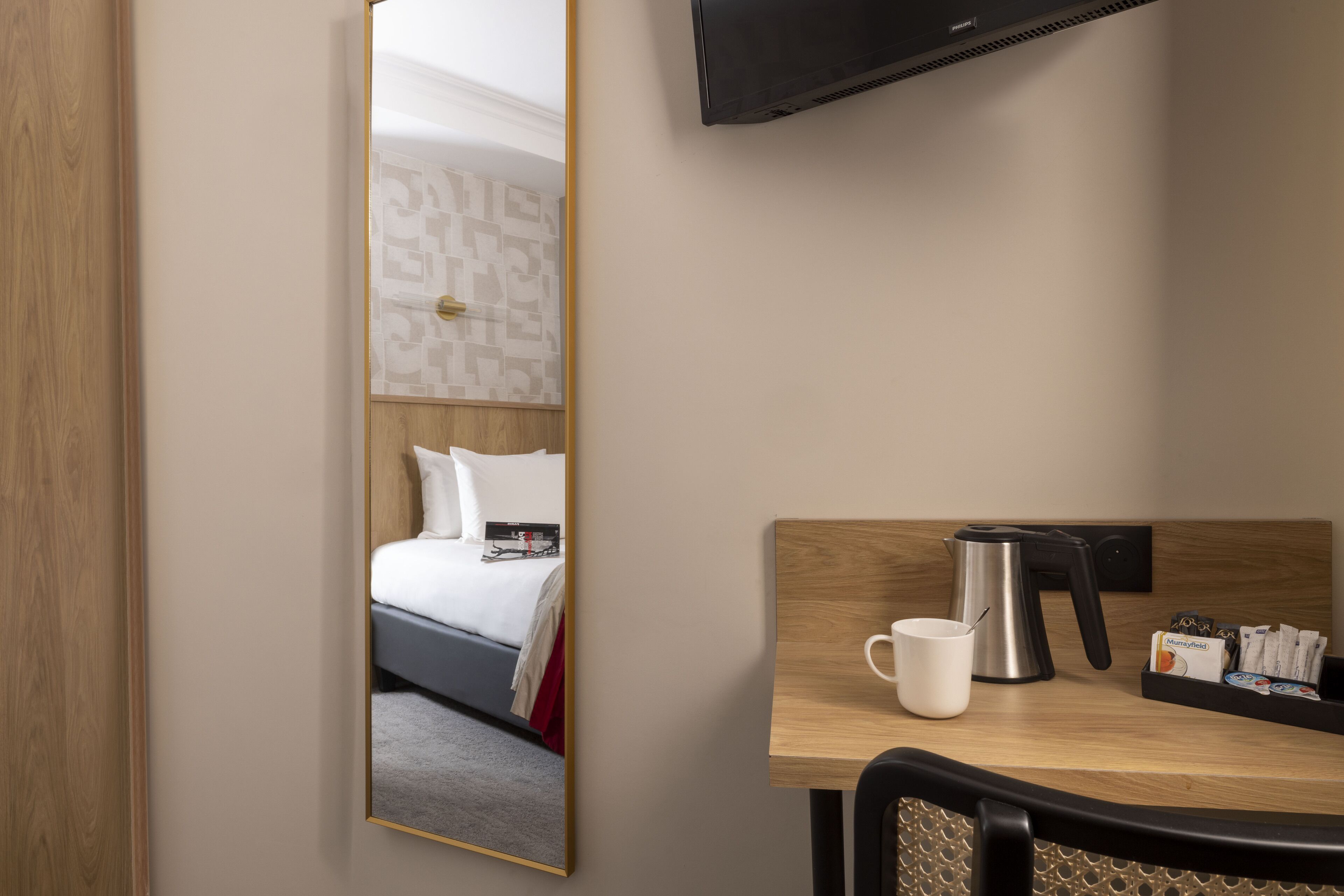 Habitación de hotel con una cama, cafetera, taza y bandeja con cápsulas de café.