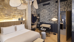 A modern hotel room with a large bed, a seating area, and a stone wall. - Abbatial Saint Germain (Paris)