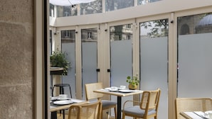 A modern outdoor dining area with wooden chairs and tables, glass partitions, and a potted plant. - Abbatial Saint Germain (Paris)