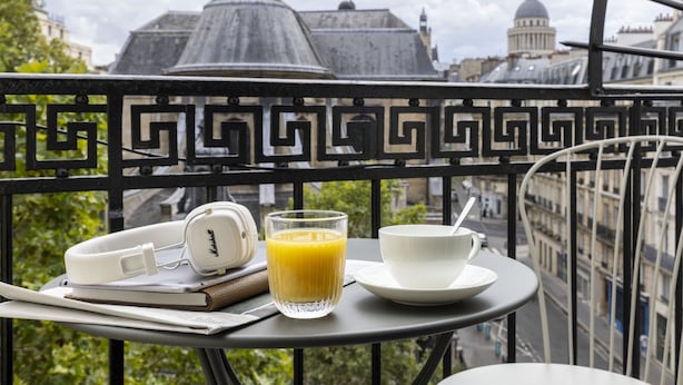 A balcony with a table set for breakfast, including a pair of headphones, a glass of orange juice, and a cup and saucer. - Abbatial Saint Germain (Paris)