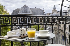 Varanda com mesa posta para o café da manhã, incluindo um par de fones de ouvido, um copo de suco de laranja e uma xícara e pires.