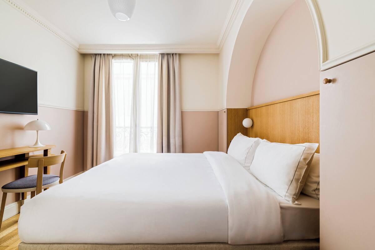 A hotel room with a large bed, a desk with a chair, a television, and a window with curtains.