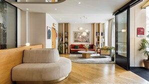 A modern hotel lobby with a curved sofa, a round coffee table, and a bookshelf. - Hôtel Oratio (Paris)