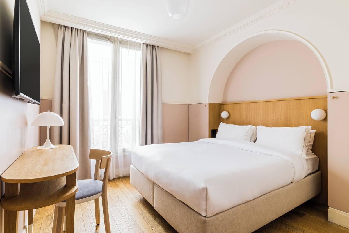 A hotel room with a bed, a desk, a chair, a television, and a window with curtains.