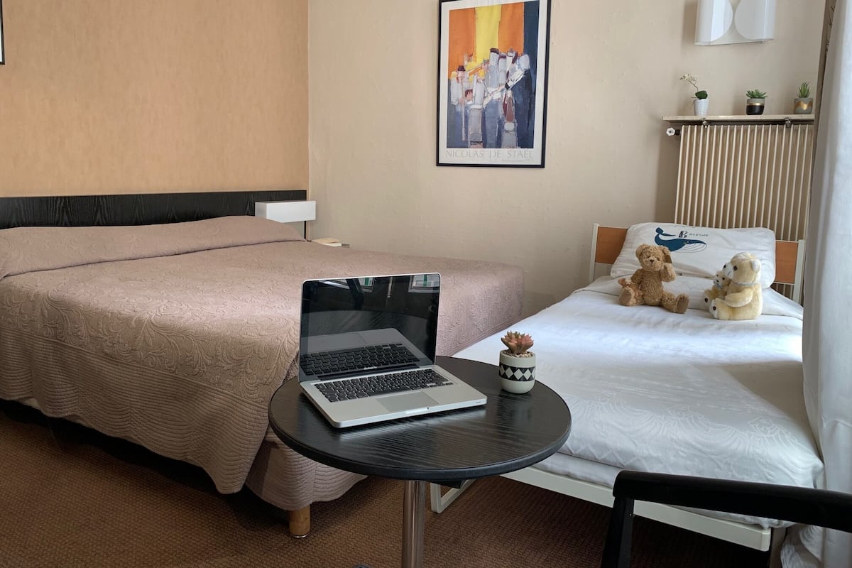 Habitación de hotel con dos camas, un ordenador portátil sobre una mesita y una obra de arte enmarcada en la pared.