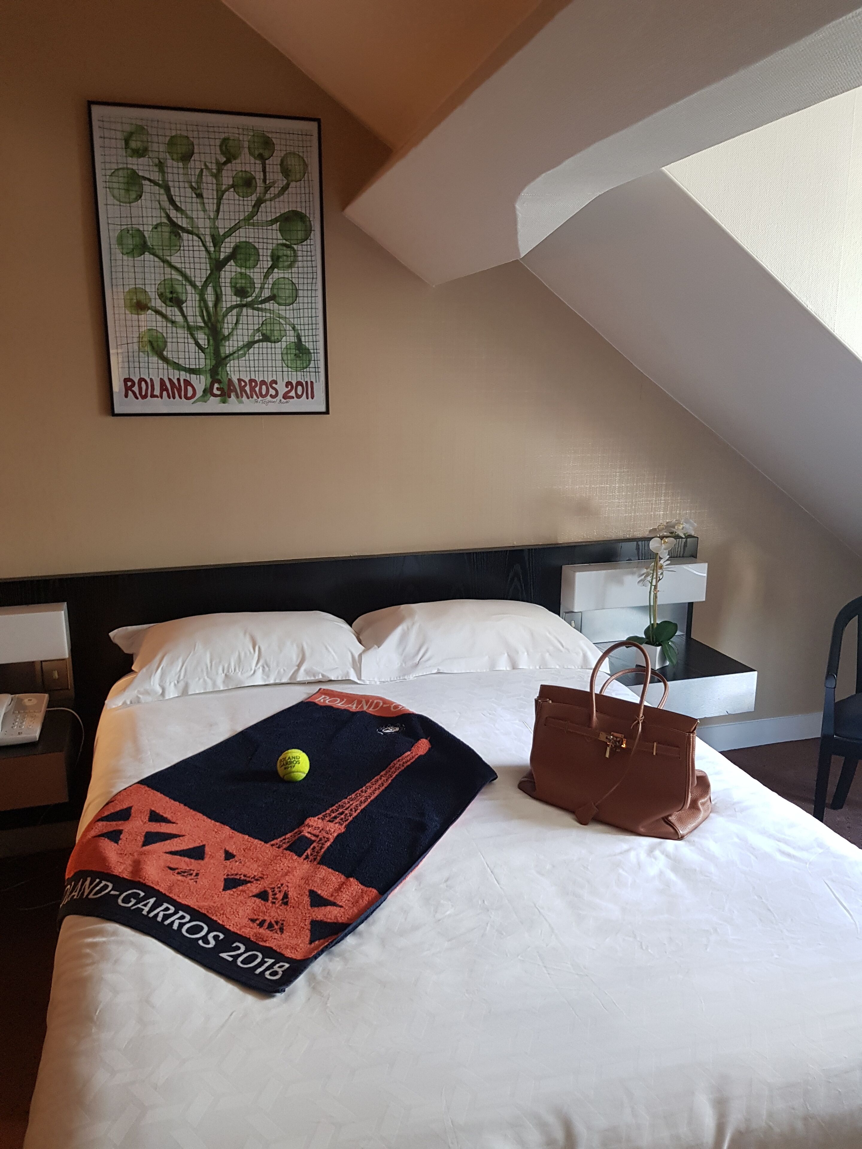 A hotel room with a bed, a nightstand, a desk, a chair, a window, and a framed picture on the wall.