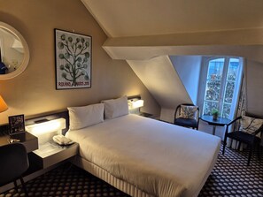 A hotel room with a large bed, bedside table, lamp, chair, and a window with a view. - Hôtel Alison (Paris)
