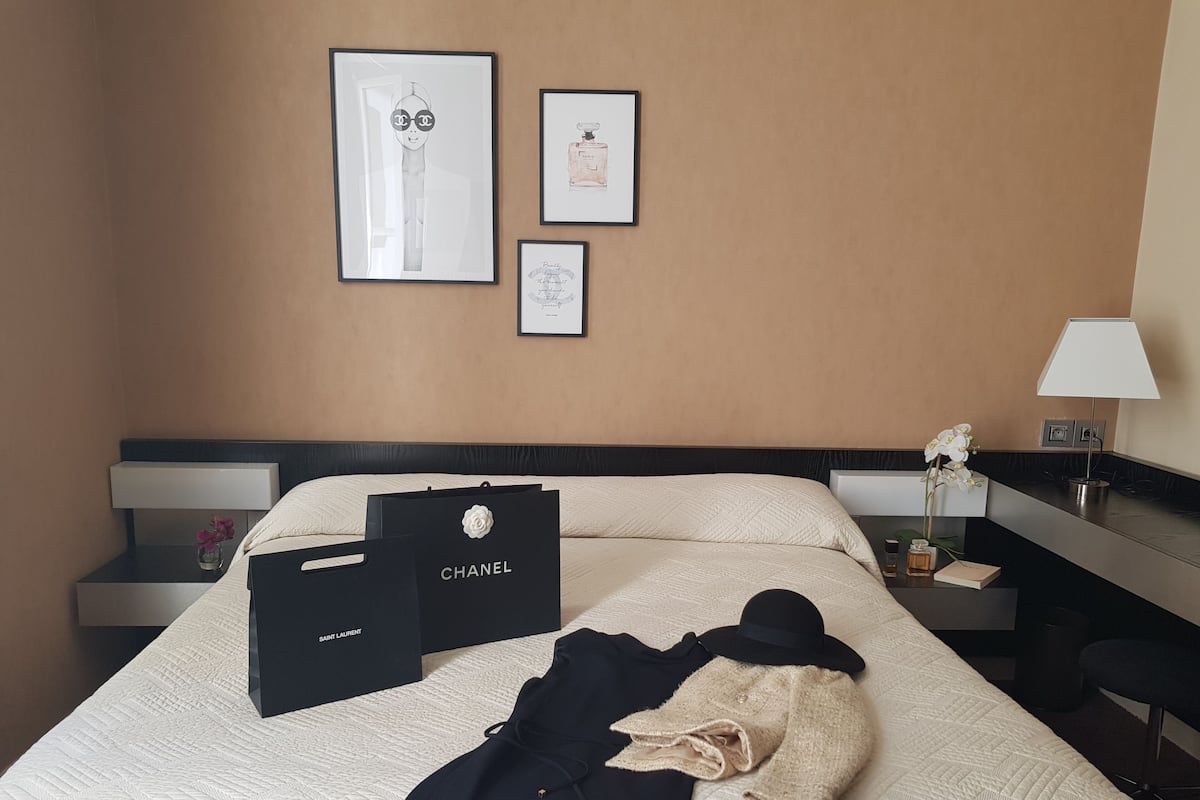 Una habitación de hotel con cama, mesita de noche, lámpara y cuadros en la pared.
