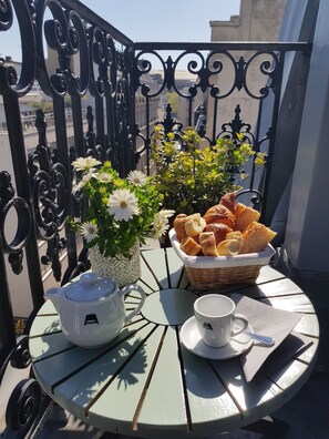 A balcony with a table set for breakfast, including a teapot, cup, saucer, basket of bread, and a potted plant with flowers. - Hôtel Alison (Paris)