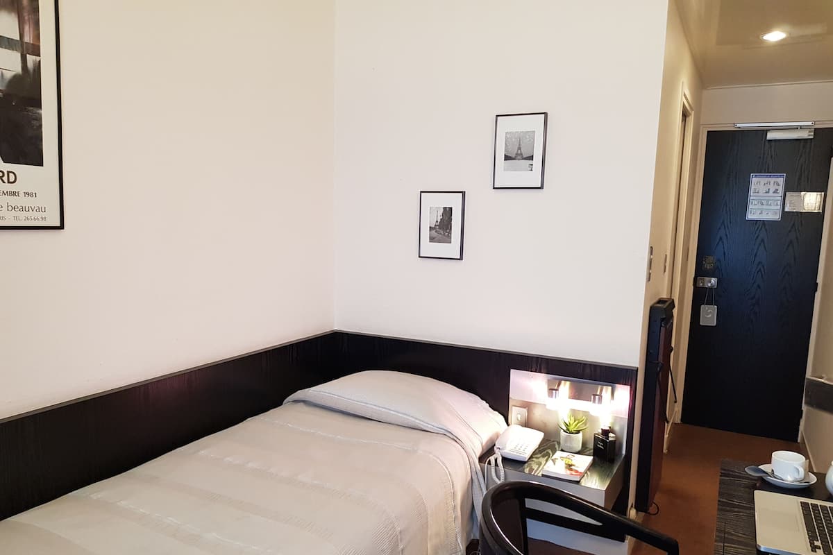 Habitación de hotel con cama, escritorio con una computadora portátil, una silla y una puerta con un letrero.