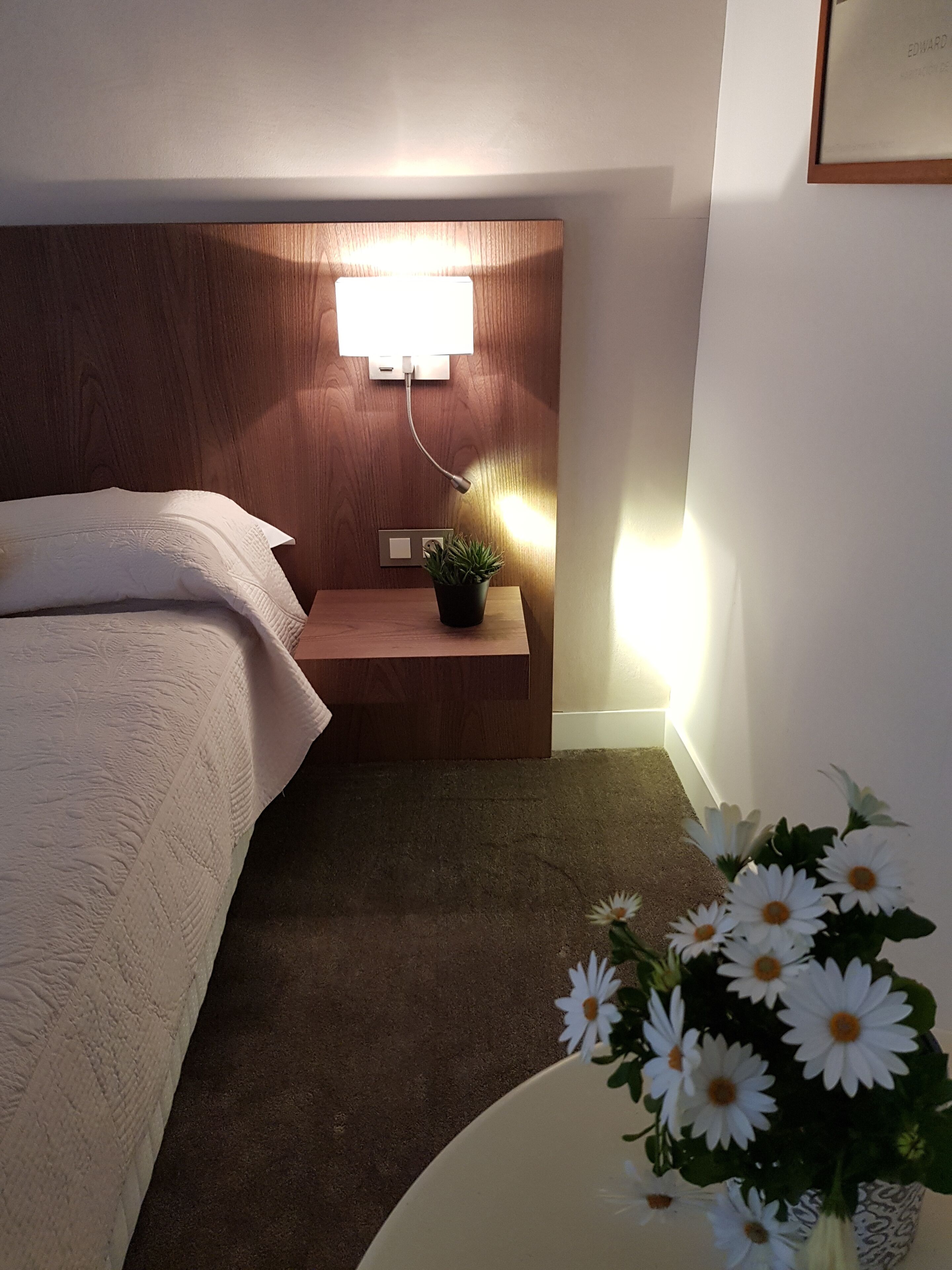 Une chambre à coucher avec une tête de lit en bois, une table de chevet ornée d’une plante et une petite table de nuit avec une lampe.