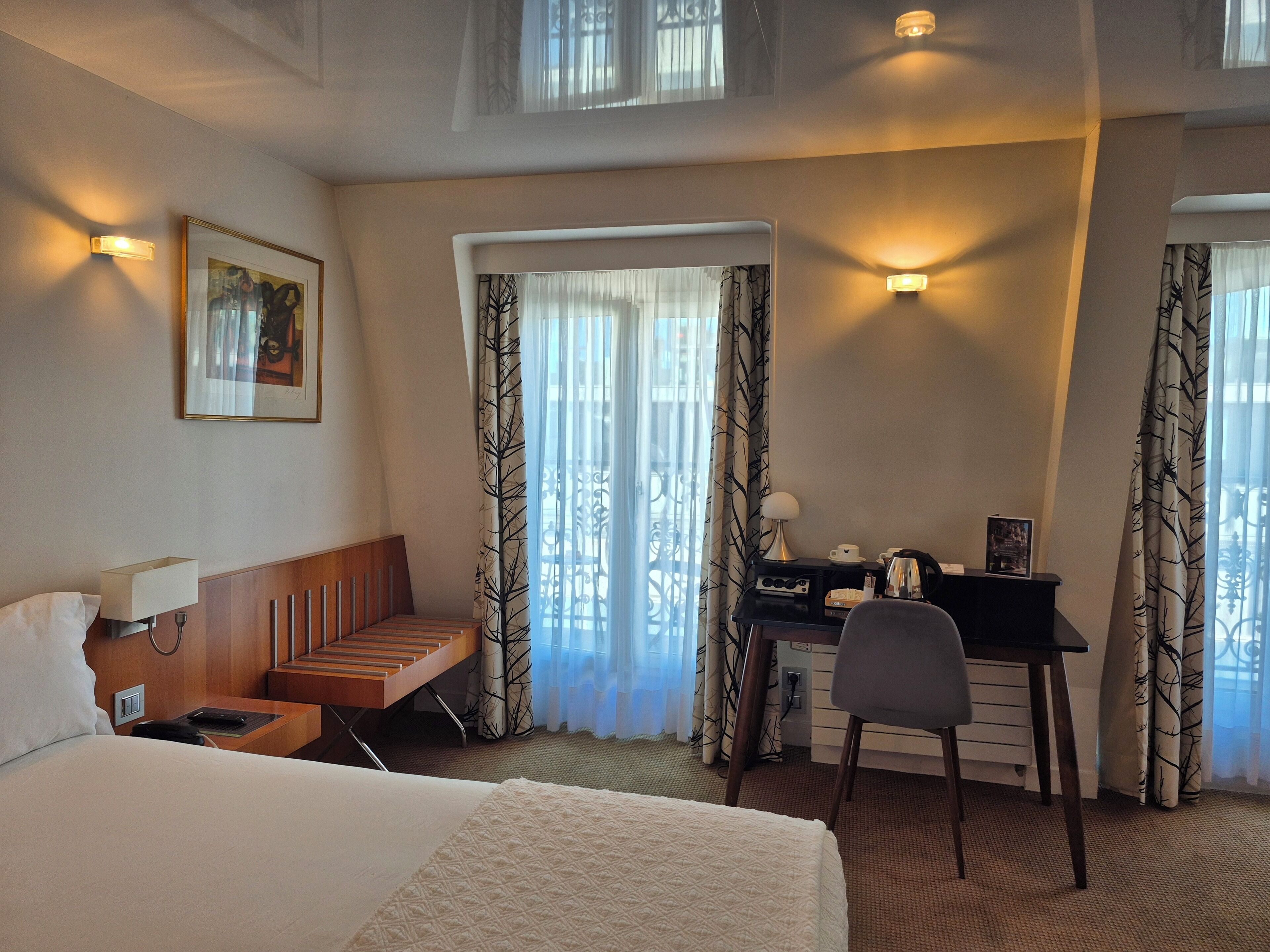A hotel room with a bed, a desk, a chair, a lamp, and a picture on the wall.